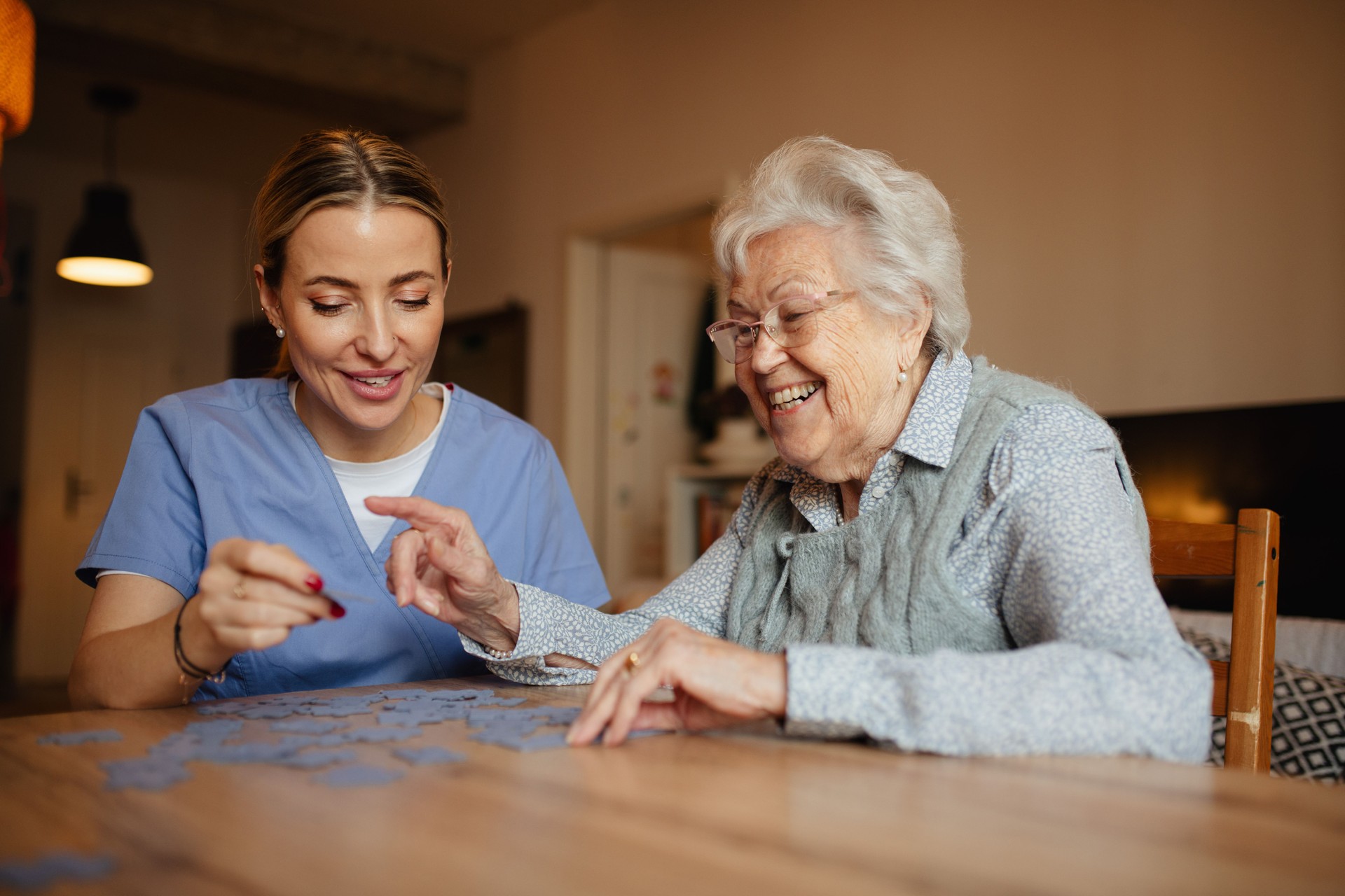 Friendly caregiver and elderly patient working on puzzle together, having fun.
