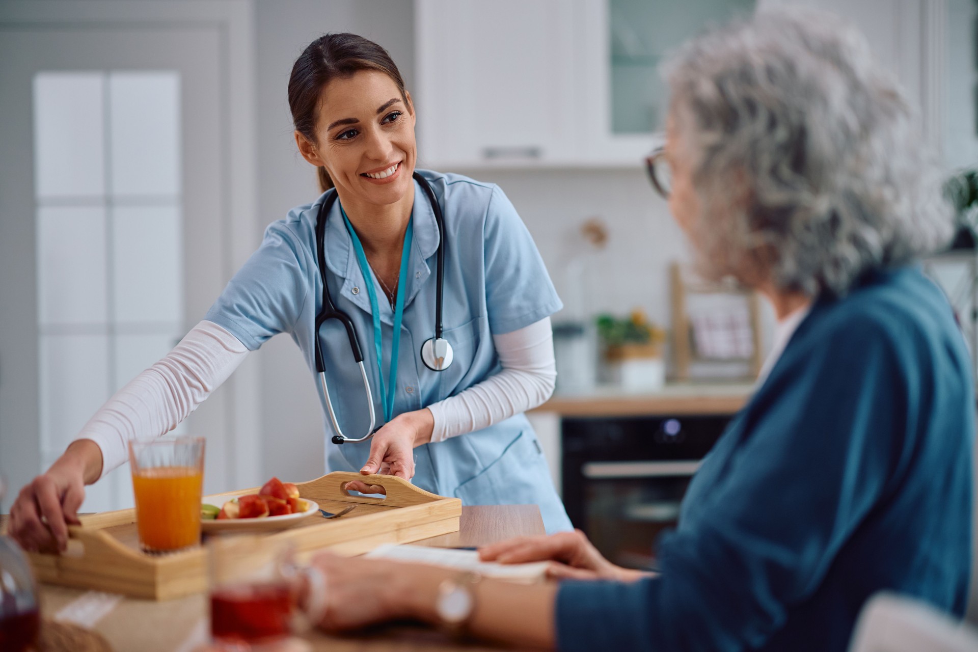 Happy visiting nurse serving fruit and juice to senior woman at home.