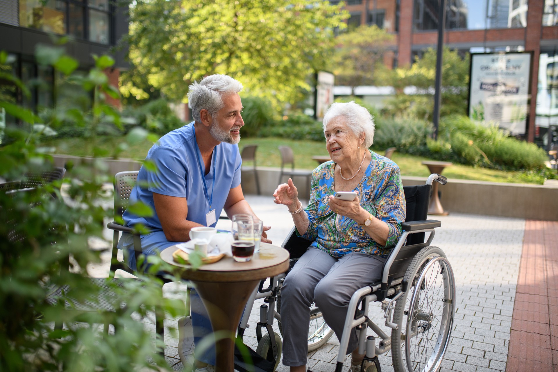 Male nurse having cup of coffee with senior patient in a wheelchair.