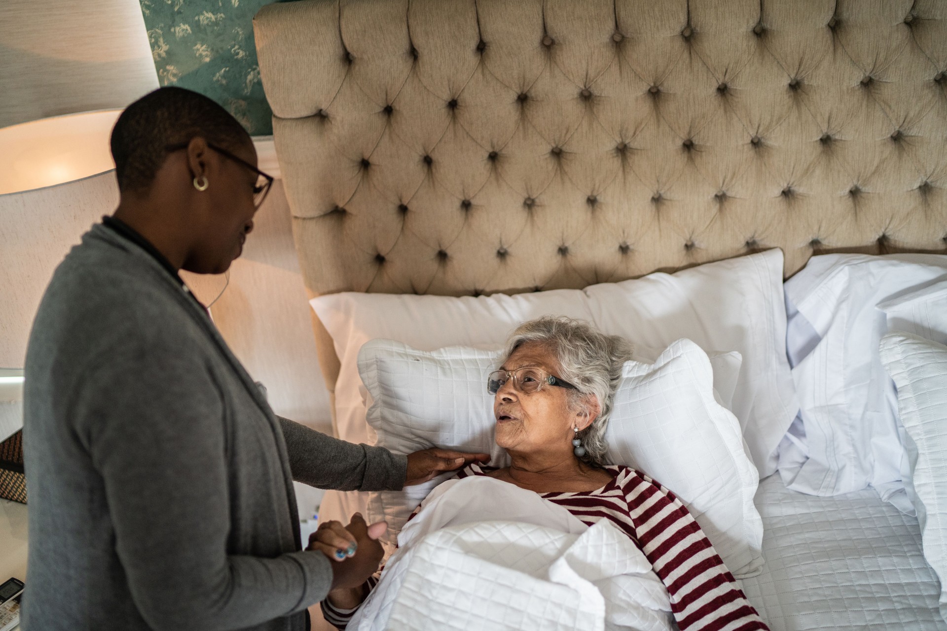 Nurse helping a senior woman lying down in the bed